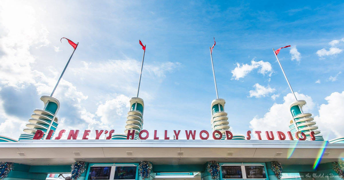 Hollywood Studios entrance sign with art deco towers and red flags, welcoming guests under a vibrant blue Florida sky.