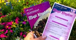Magic Kingdom guidemap and times guide held up, surrounded by vibrant flowers—your ticket to an epic Walt Disney World adventure.