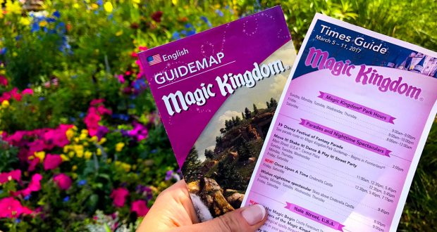 Magic Kingdom guidemap and times guide held up, surrounded by vibrant flowers—your ticket to an epic Walt Disney World adventure.