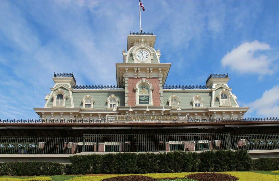 Magic Kingdom’s classic train station and clock tower, framed by lush bushes and bright skies, is an iconic Disney World photo spot.