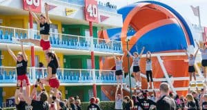 Cheerleaders show off thrilling stunts in front of a vibrant Disney Resort building with giant numbers and a blue-orange ball.