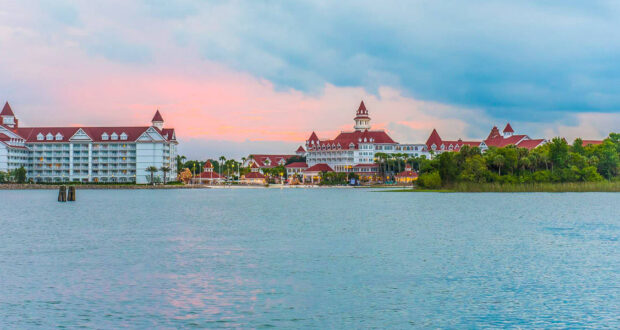 Red-roofed, lakeside Disney resort glows at sunset, nestled in greenery—an enchanting escape moments from the theme park magic.