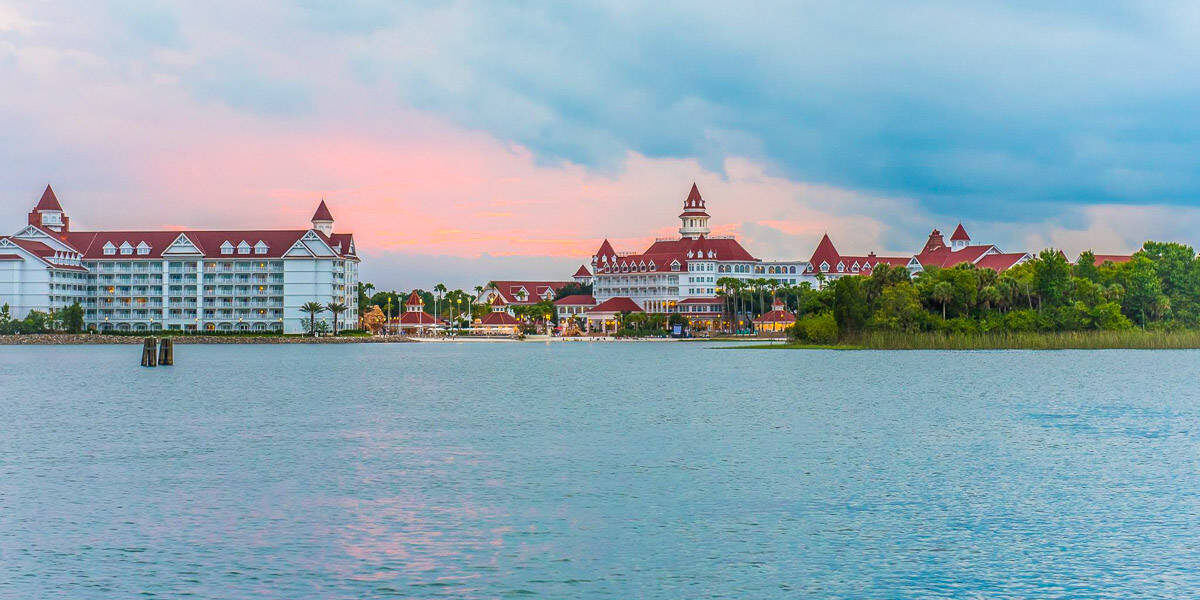 Red-roofed, lakeside Disney resort glows at sunset, nestled in greenery—an enchanting escape moments from the theme park magic.
