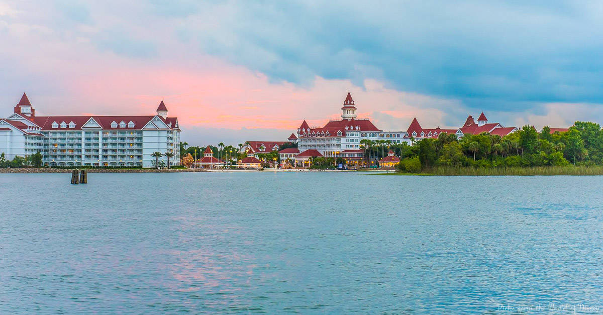Red-roofed, lakeside Disney resort glows at sunset, nestled in greenery—an enchanting escape moments from the theme park magic.