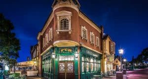 A lively, warmly lit British pub on a Disney street corner at night, outdoor seating, deep blue sky—evoking Disney dining magic.