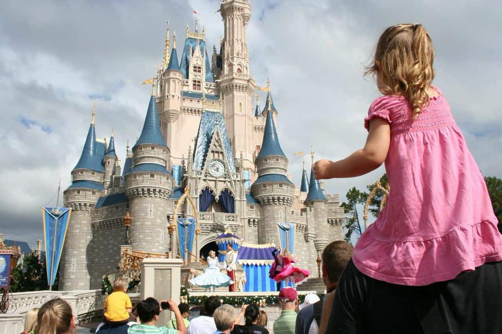 A young guest rides on shoulders, enjoying a dazzling castle show amid the lively crowds at Walt Disney World.