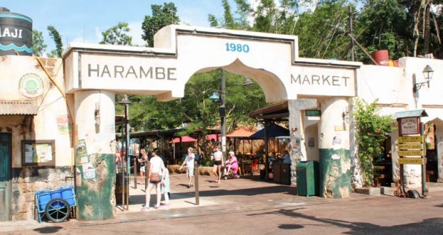 Harambe Market entrance arch at Disney's Animal Kingdom, bustling with guests, lush trees, and vibrant market stalls beyond.