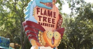 Flame Tree Barbecue’s vibrant sign with playful animal art, nestled in lush greenery, invites Disney World guests to feast.