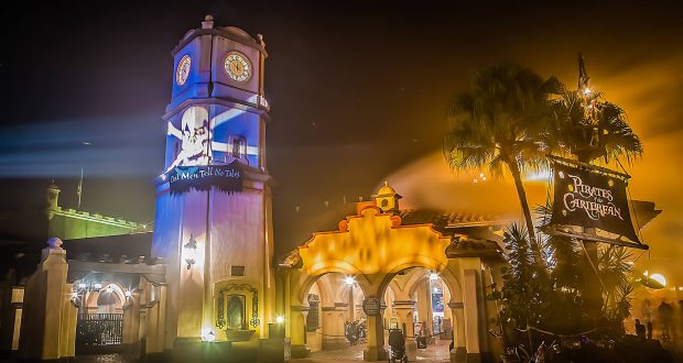 Pirates of the Caribbean at Walt Disney World glows at night with a dramatic skull on the clock tower and inviting, warm lights.