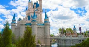 Cinderella Castle with blue turrets, surrounded by water and greenery beneath a partly cloudy sky at Walt Disney World.