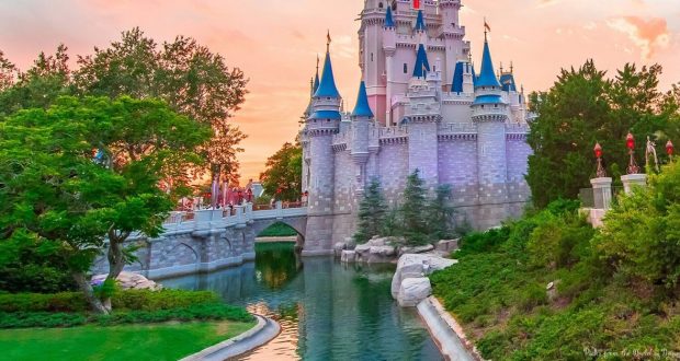 A magical castle by a shimmering moat, framed by lush trees at sunset, evokes Disney World’s enchanting vacation vibe.