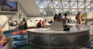 Disney fans chat in a bright, modern lounge with geometric windows and bold carpets, trading Vacation Club tips for magical visits.