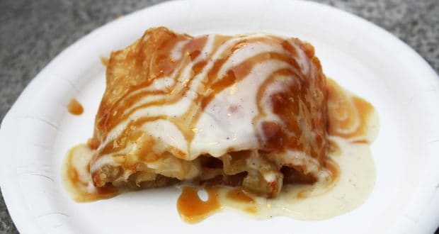 Lasagna slice with white and brown sauce on a paper plate—a tasty treat after touring Epcot’s Karamell-Küche.