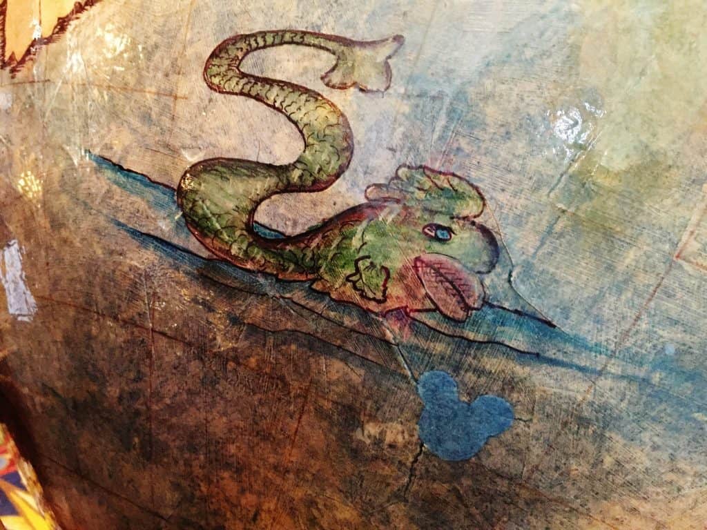 A green sea serpent appears on a vintage map next to a blue Mickey icon, teasing a secret adventure within Disney’s Resorts.