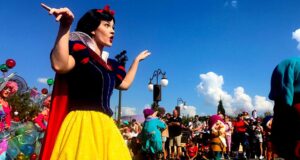 Snow White delights guests in a vibrant parade, waving amid beloved characters and fans during a magical Disney celebration.