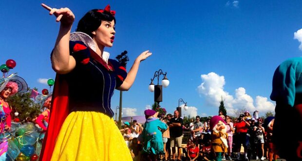 Snow White delights guests in a vibrant parade, waving amid beloved characters and fans during a magical Disney celebration.