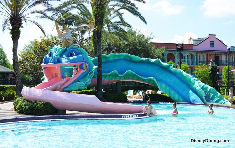 Kids splash in a pool by a sea serpent waterslide, surrounded by palms, soaking up Disney World Resort’s signature magic.