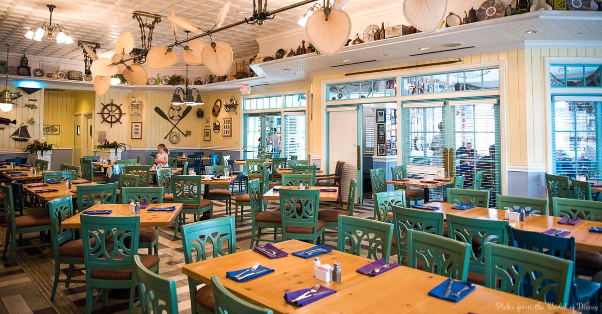 Nautical eatery with teal chairs, wooden tables, ocean accents; Disney World vibes, relaxed and nearly empty dining area.
