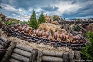 The Seven Dwarfs Mine Train twists through rugged rocks, lush trees, and a bridge beneath clouds at Magic Kingdom—pure Disney thrills!.