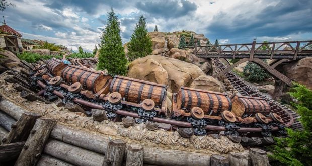 The Seven Dwarfs Mine Train twists through rugged rocks, lush trees, and a bridge beneath clouds at Magic Kingdom—pure Disney thrills!.
