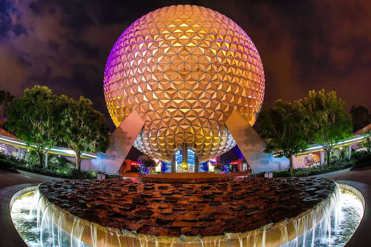Spaceship Earth at Epcot shines in vibrant night lights, with dancing fountains ahead, creating pure Disney World magic.