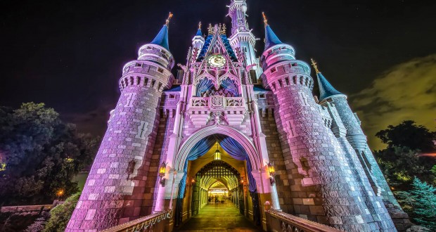 Cinderella Castle dazzles at night with vibrant lights, greeting Magic Kingdom guests from the entrance bridge at Disney World.