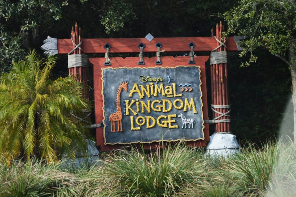 Disney’s Animal Kingdom Lodge sign with giraffe and zebra art in lush greenery—where Disney magic meets African wildlife adventure.