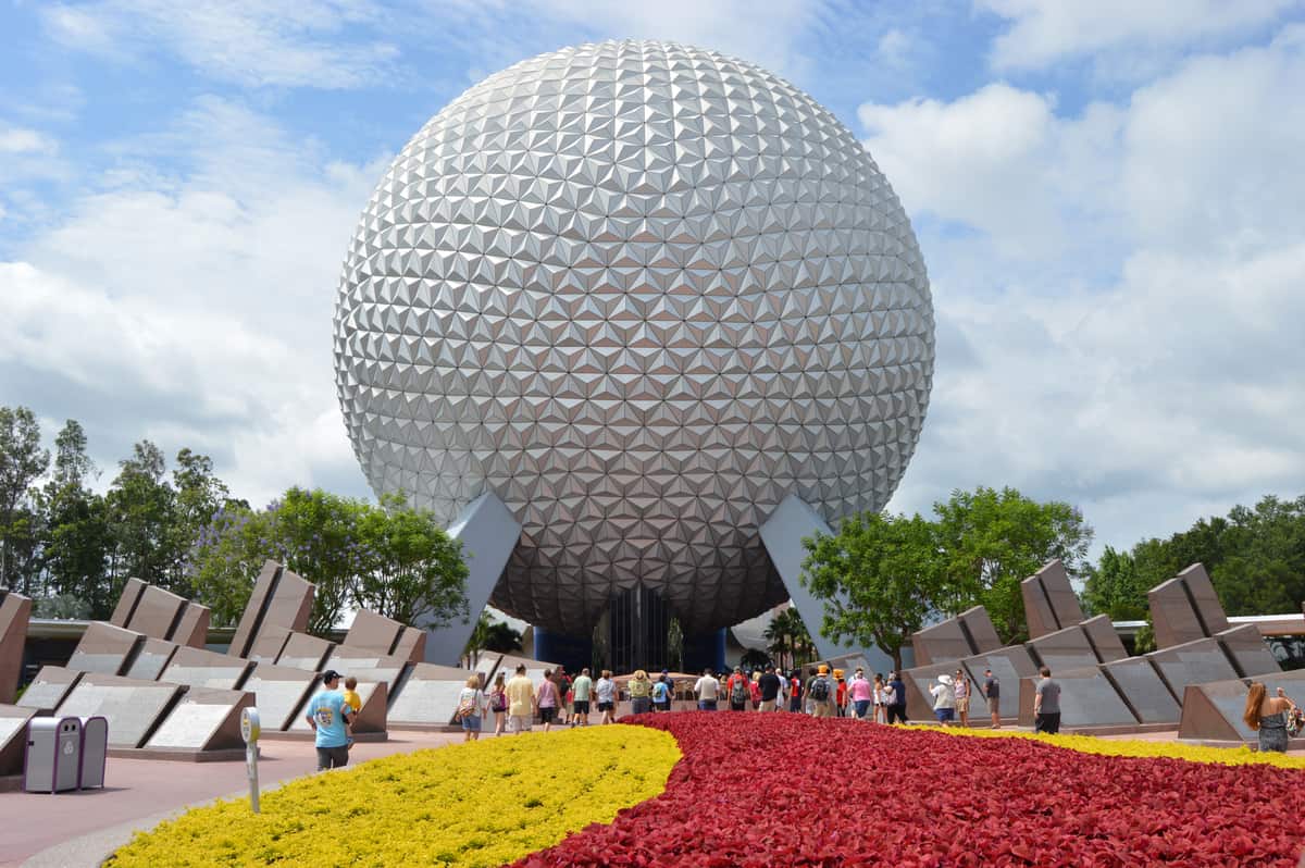 Guests flock toward Epcot’s iconic geodesic sphere, framed by vibrant gardens—an unforgettable Disney park experience.