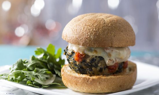 A cheesy veggie burger on a bun with green salad, plated and ready for hungry Disney park-goers craving a delicious snack.