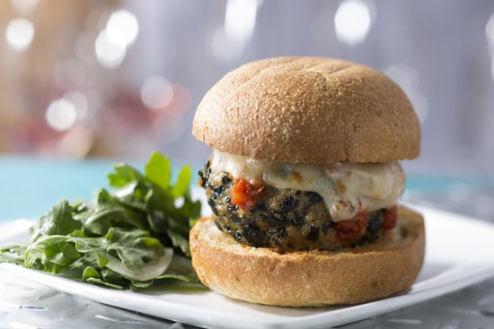 A cheesy veggie burger on a bun with green salad, plated and ready for hungry Disney park-goers craving a delicious snack.