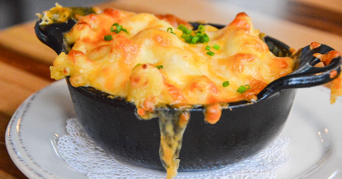 Classic Disney World-style baked mac and cheese, topped with melted cheese and chives, served in a black dish on a white plate.