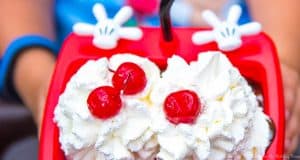 A vibrant red Walt Disney World bowl topped with whipped cream, cherries, and a straw—an iconic park snack to savor!.