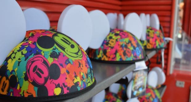 Vibrant Mickey Mouse ear hats with fun designs line a shelf against a red wall—must-haves for your Hollywood Studios adventure.