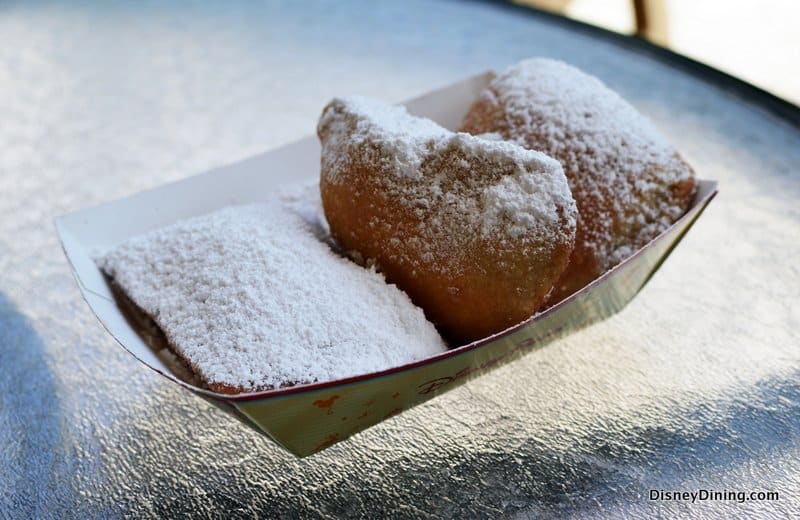Three classic beignets dusted with powdered sugar, served in a paper tray—an iconic Disney resort snack found at moderate resorts.