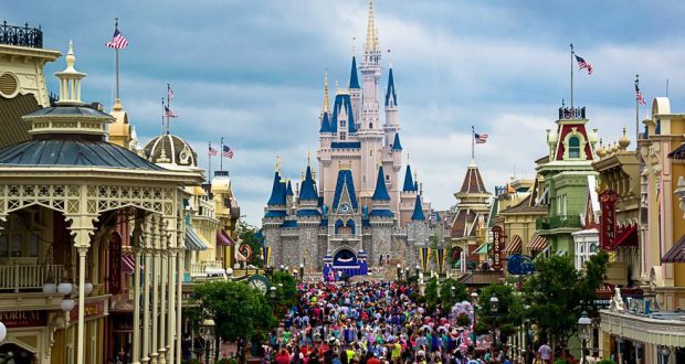 Guests fill Main Street, U.S.A., heading toward Cinderella Castle at Magic Kingdom under a cloudy sky.