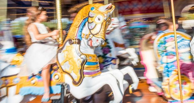 A young guest in a white dress enjoys the spinning carousel at Magic Kingdom, vibrant lights swirling in true Disney style.