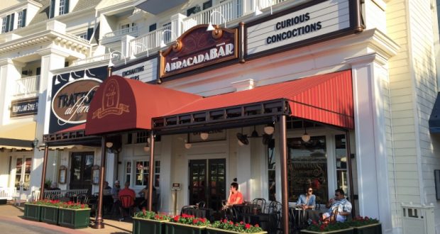 Guests unwind beneath a vibrant red awning at AbracadaBar, enjoying sunny boardwalk views at Walt Disney World.