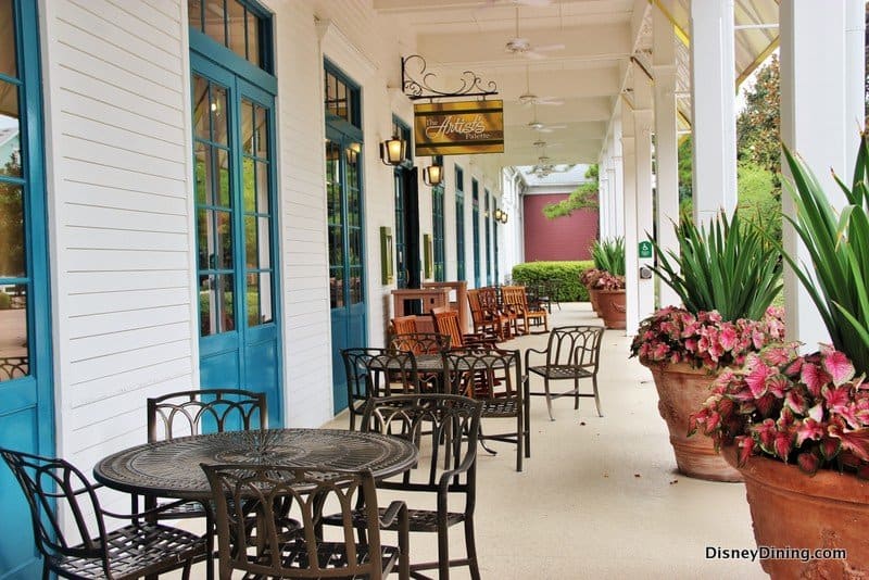 Charming patio with black metal tables and chairs, potted plants, and blue doors at Disney’s Saratoga Springs Resort.