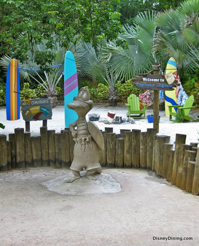 Goofy strikes a pose with his surfboard at Typhoon Lagoon, surrounded by vibrant boards and chill chairs—a photo op for Disney fans.