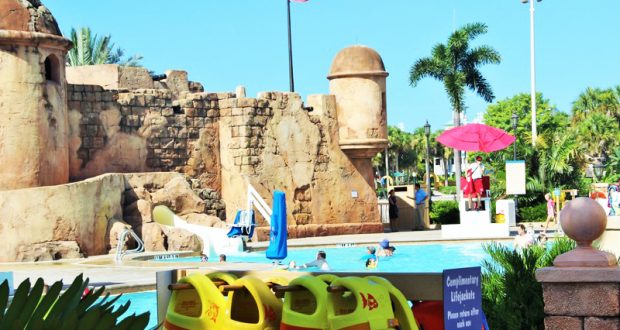 Caribbean Beach Resort pool with iconic stone castle, swaying palms, lifeguard, and yellow life jackets—relax Disney style!.