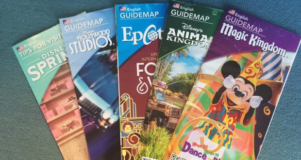 Disney World guidemaps fanned out on blue, showcasing vibrant covers—your ticket to every magical secret in the parks.