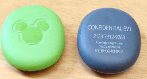 A green Disney Magic Band and a gray “CONFIDENTIAL EV1” device on wood tease potential new tech coming to Walt Disney World.