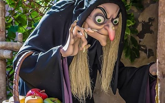 The Evil Queen in her witch form with a basket of apples crouches under a wooden beam, evoking Seven Dwarfs Mine Train vibes.