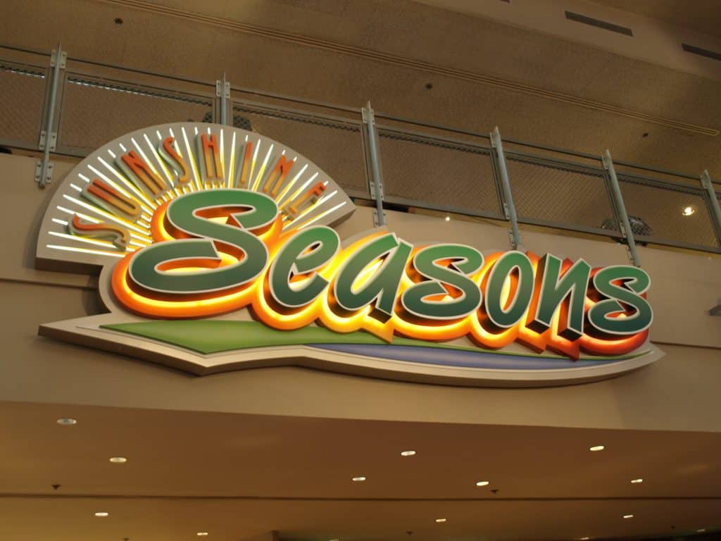 Sunshine Seasons" sign with vibrant sunburst greets guests at EPCOT, inviting you into this colorful Disney dining spot.