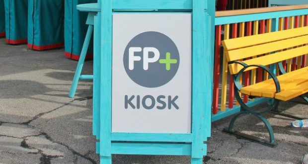 FP+ KIOSK sign at Walt Disney World sits beside a yellow bench on worn pavement, marking the legacy of the old FastPass system.