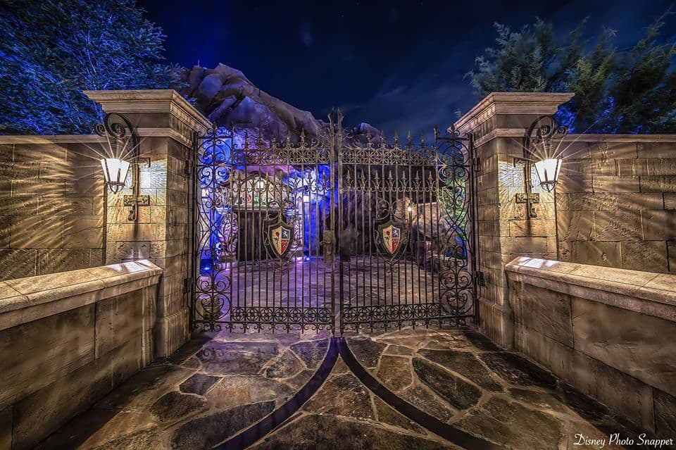 Decorative iron gate with glowing lanterns at night, welcoming guests to Be Our Guest Restaurant in Magic Kingdom.