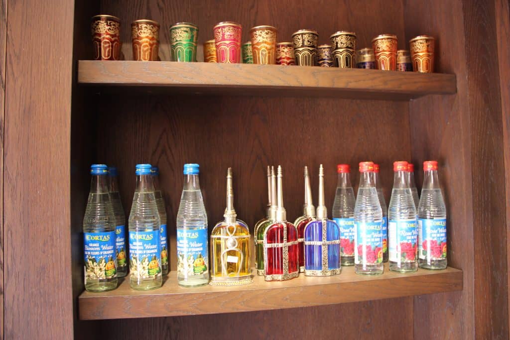 Elegant glass bottles and EPCOT-style glasses line wooden shelves, with perfume bottles center stage, evoking World Showcase magic.