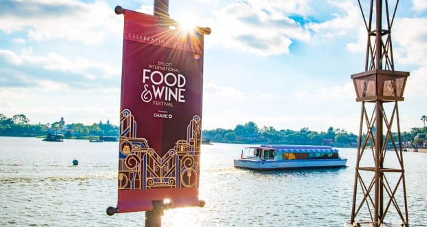Epcot Food & Wine Festival red banner by the lake, boat cruising in the background under sunny skies at Walt Disney World.
