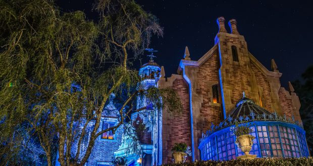 The Haunted Mansion aglow with eerie blue lights at night, trees and a star-filled sky evoke classic Disney World after-dark magic.