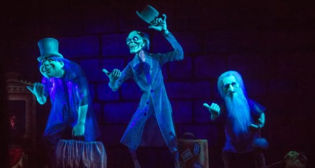 The iconic blue Hitchhiking Ghosts from Disney’s Haunted Mansion pose with hats and suitcases against a shadowy backdrop.